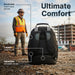 Targus Drifter backpack shown from the rear at a construction site, with a worker in a hard hat and safety vest in the background. Callouts identify three comfort features: breathable mesh back panel, lumbar padding, and adjustable shoulder straps.